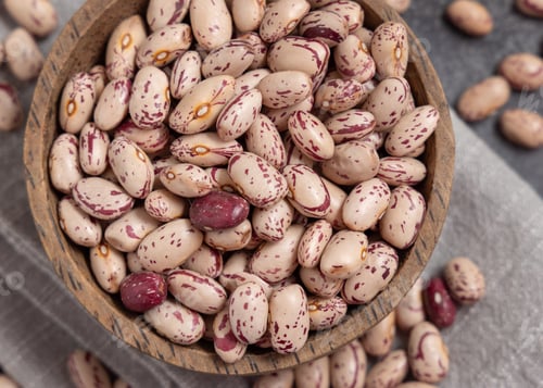 Preview: Wooden bowl full of dried pinto beans on napkin top view. Traditional Latin American legumes