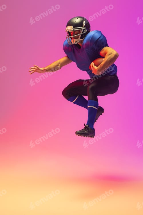 Preview: Caucasian male american football player holding ball with neon pink lighting