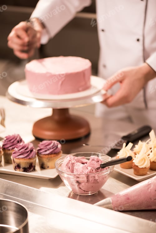 Preview: cropped shot of confectioner making cake in restaurant kitchen
