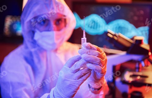 Preview: Nurse in mask and white uniform, holding syringe and sitting in neon lighted laboratory
