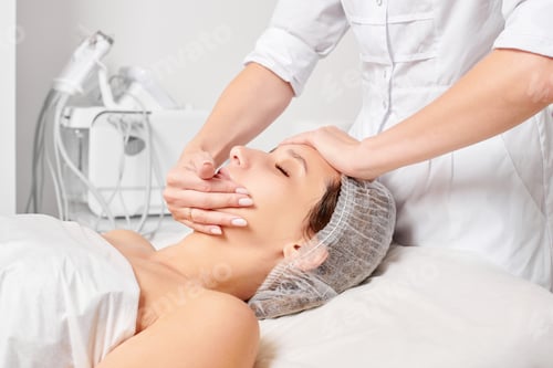 Preview: Cosmetologist rubbing moisturizing cream mask into woman face skin for rejuvenation in beauty salon