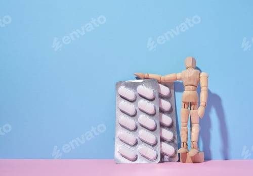 Preview: Oval pills in a blister pack and a wooden puppet man on a blue background