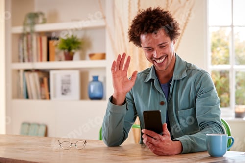 Preview: Man Sitting At Table At Home Using Mobile Phone For Video Call