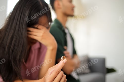 Preview: Unhappy couple facing emotional moment, woman holding wedding ring in hand, divorce discussion.