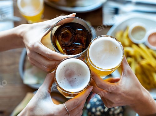 Preview: Hand's of young friends toasting with beer while having fun in a restaurant.