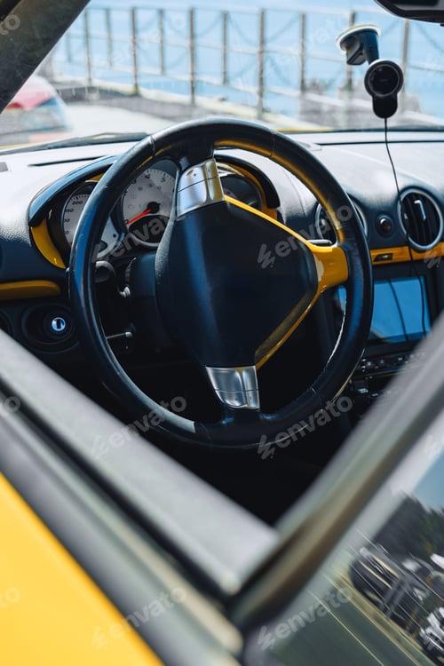 Preview: Car interior with a yellow steering wheel and dashboard near the coast on a sunny day