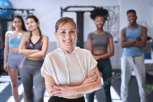 Preview: Woman smiling while standing in front of a group of sportive people at the gym.
