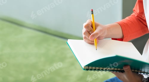 Preview: Close up hand of male teenager writing with pencil on notebook at campus