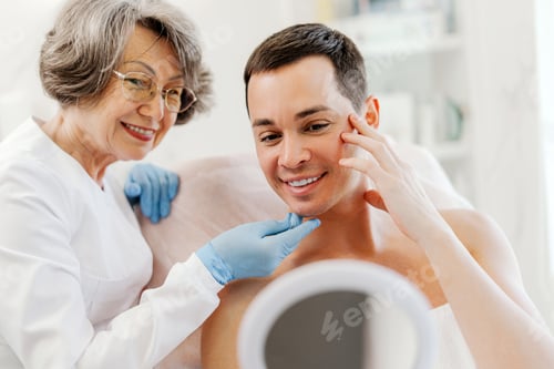 Preview: Smiling attractive man and senior smiling cosmetologist doctor talking, looking in mirror