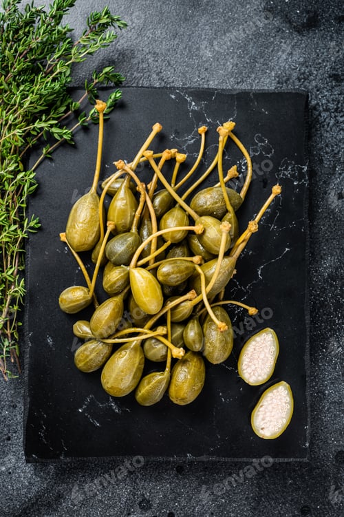 Preview: Pickled canned capers on a marble board. Black background. Top view