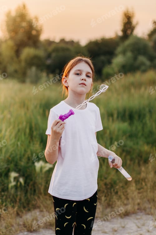 Preview: Little girl wearing casual white t-shirt mock up and walking alone in summer meadow with scenic path