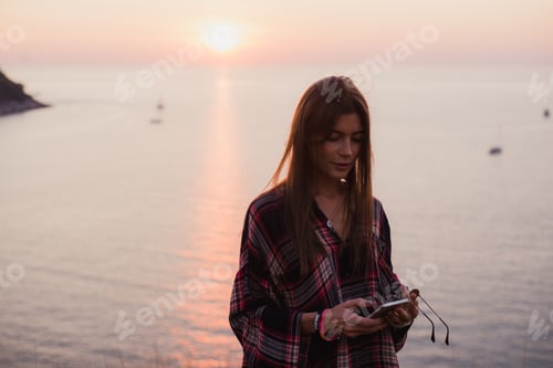Preview: woman texting on smart phone on the beach during sunset