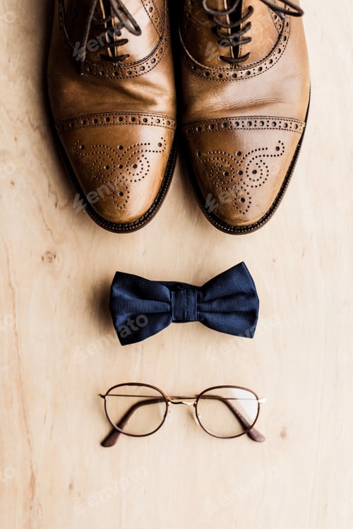 Preview: top view of shoes, tie bow and glasses on wooden floor