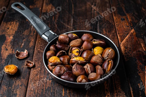Preview: Roasted chestnuts nuts in a pan. Wooden background. Top view