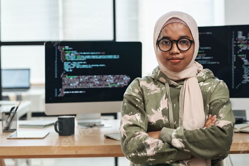 Preview: Young IT engineer in hijab sitting against computer screens with coded data