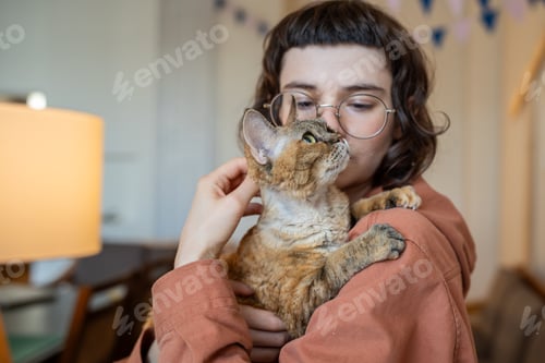 Preview: Pet lover holding in hands, stroking purring of pleasure cat Devon Rex, looking with great love