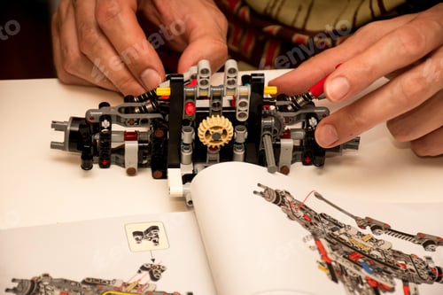 Preview: Hands making a piece of machinery from plastic pieces blocks constructor details according to manual