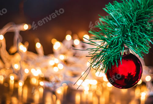 Preview: Selective focus shot of a red Christmas ball on a pine tree with lights on the background