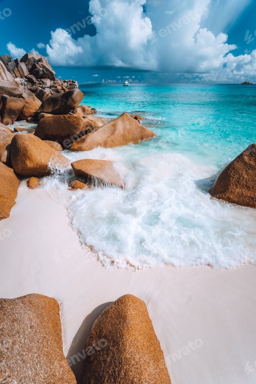 Preview: Foam wave between rocks on Grand Anse beach, La Digue, Seychelles. White clouds, crystal clear ocean