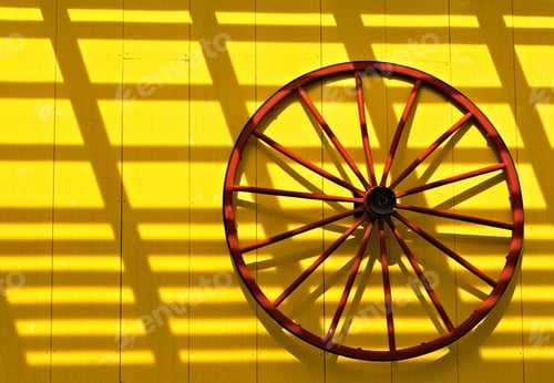 Preview: Red wagon wheel on a yellow wall with latticed shadow on it