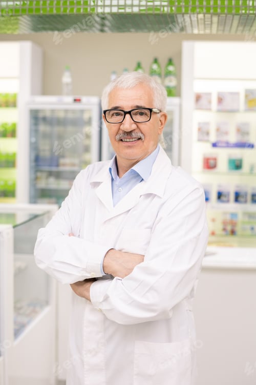 Preview: Aged drugstore worker in whitecoat and eyeglasses crossing his arms by chest