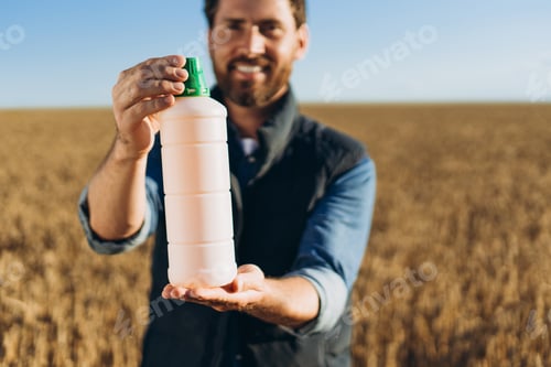 Preview: Farmer holding fertilizer bottle in wheat field smiling at camera selective focus
