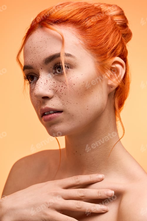 Preview: Stylish young woman with orange hair and freckles poses gracefully against a warm backdrop