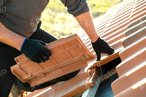 Preview: Closeup of worker hands installing yellow ceramic roofing tiles mounted on wooden boards covering