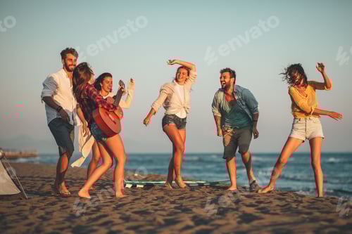 Preview: Happy friends sitting on the beach singing and playing guitar during the sunset