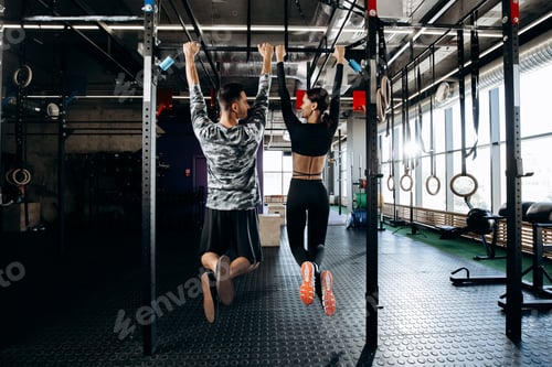 Preview: Slender girl and athletic man dressed in sports clothes are pulling up on the bar in the gym