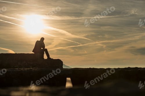 Preview: Pensive businessman in elegant suit sitting on a ruins of a cast