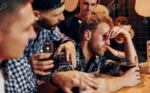 Preview: Sad man feels bad. Group of people together indoors in the pub have fun at weekend time