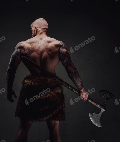 Preview: Rear view of healthy tattoed warrior in fur with axe on a dark background