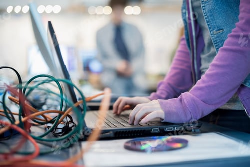 Preview: A person using a laptop computer. Disc and wires on the counter. Repair shop.