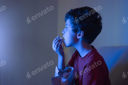 Preview: Child watching a movie totally engrossed in television sitting at home eating popcorn.