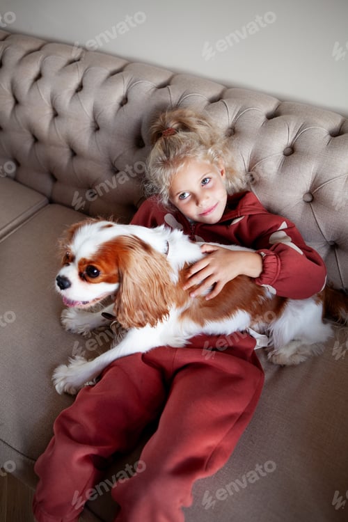 Preview: Smiling Girl Cuddling Dog on Sofa Indoors