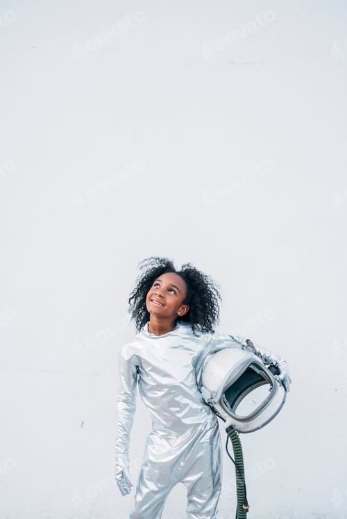 Preview: Portrait of smiling little girl wearing space suit in front of white background looking up