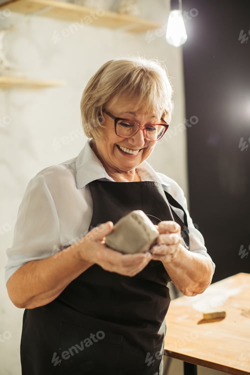 Preview: Senior woman enjoying pottery class, shaping clay with a smile