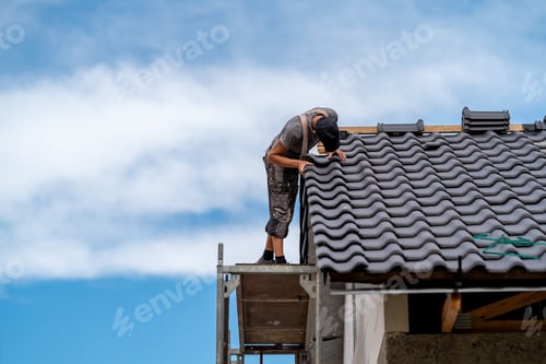 Preview: craftsman on scaffolding installs ceramic tile on the roof of a family home, copy space