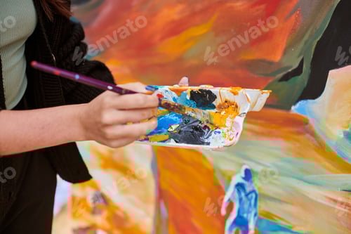 Preview: Female painter hand dips paintbrush into palette of colorful paints for live painting of picture