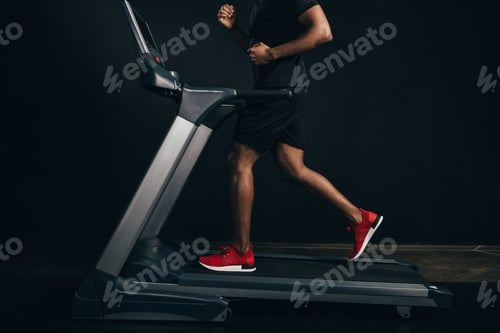 Preview: cropped shot of african american sportsman running on treadmill on black