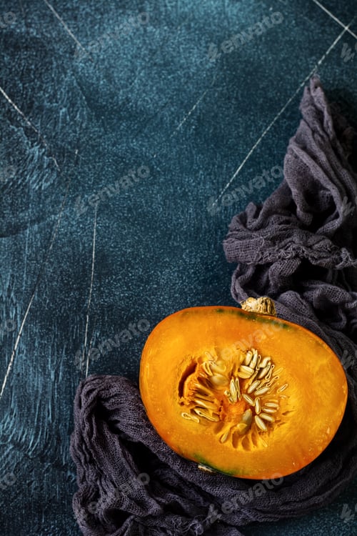 Preview: Fresh cut in half pumpkin with gray napkin on old stone dark blue background. Halloween concept. Top