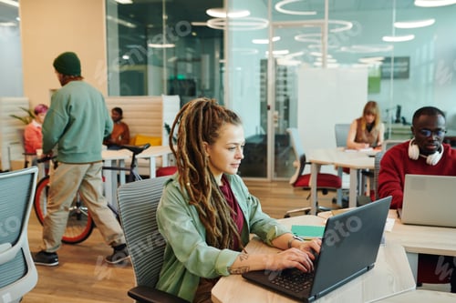 Preview: Serious young female office manager in casualwear using laptop by workplace