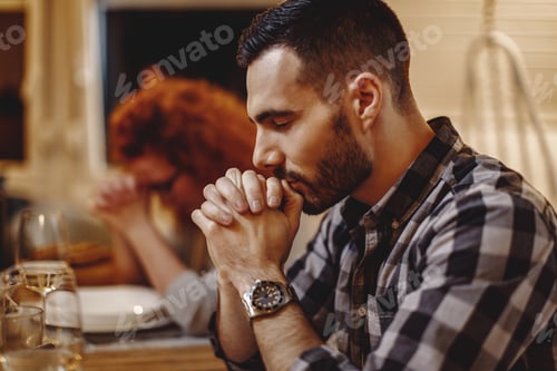 Preview: Grateful man praying before a meal at dining table.