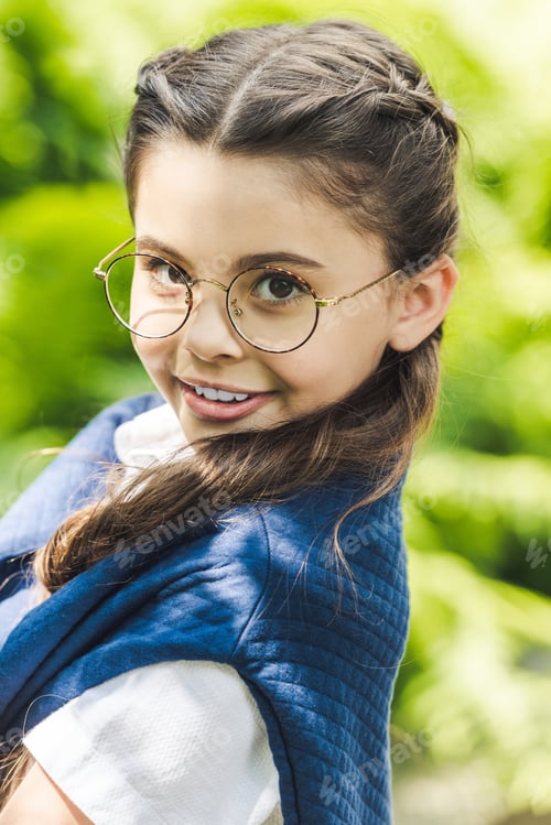 Preview: close-up portrait of adorable schoolgirl in white shirt and jumper over shoulders looking at camera