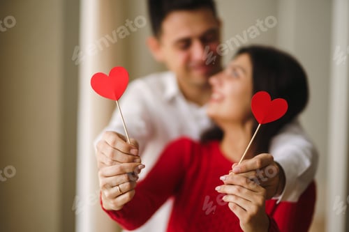 Preview: Young cheerful couple in love holding red hearts over eyes and smiling. Valentines day concept.