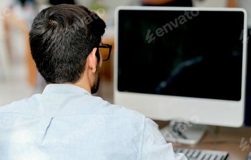 Preview: Back view of business man with blue shirt look at the monitor of computer during work at home.