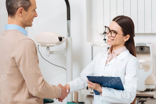 Preview: side view of optometrist with notepad and patient shaking hands in hospital