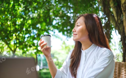 Preview: Portrait image of a woman holding and drink coffee while working on laptop computer in the outdoors