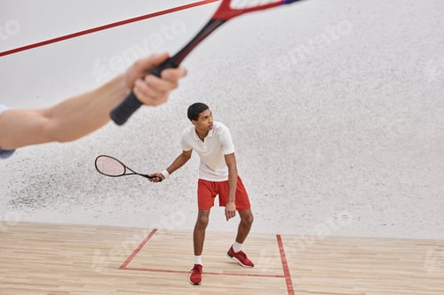 Preview: african american man in sportswear playing with friend inside of squash court, blurred foreground